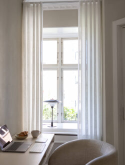 Hvide transparente stofgardiner fra Luxaflex® , som hænger inde på et kontor.